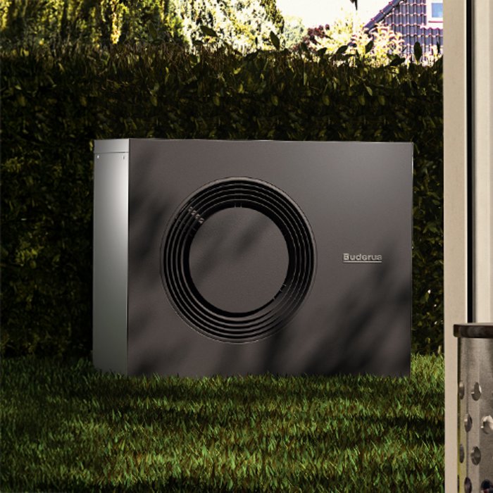 Eine Wärmepumpe steht einem Stein.Im Hintergrund ist eine blaue Holzfassade zu sehen.