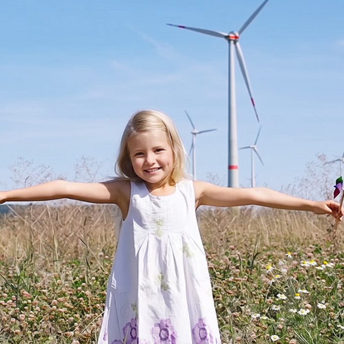 Ein Mädchen steht auf einer Wiese mit zwei kleinen Windrädern in der Hand und lächelt. 