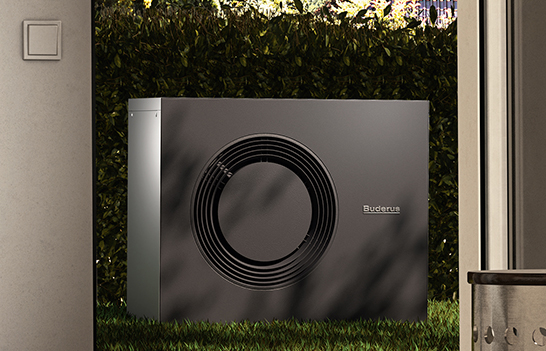 Eine Wärmepumpe steht einem Stein. Im Hintergrund ist eine blaue Holzfassade zu sehen.